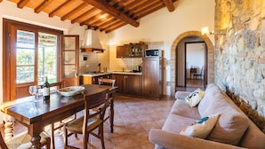 A rustic kitchen with wooden beams, a stone wall, and a cozy dining area with a table and chairs. - Raffaello Apartment ~ LE FRAINE (New Opening 2022) (Santa Luce)