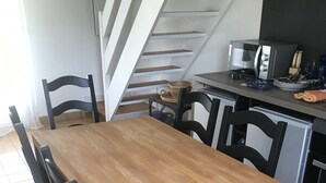 Un comedor con mesa de madera y sillas negras, una cocina con microondas, y una escalera que sube.