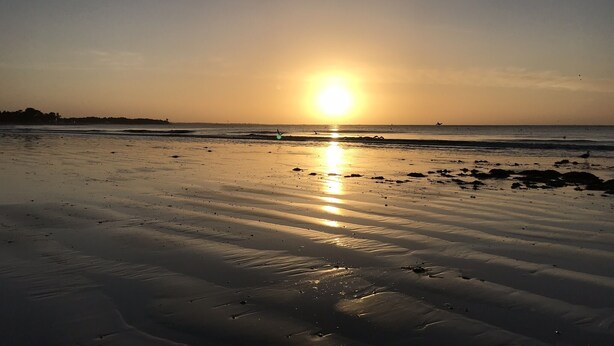Una playa al atardecer, con el sol bajo en el horizonte, proyectando un resplandor cálido sobre la arena.