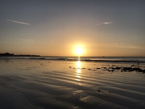 Une plage au coucher du soleil, le soleil étant bas à l’horizon et projetant une lumière chaude sur le sable.
