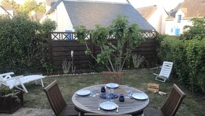 Una mesa redonda de madera dispuesta para cuatro personas, con sillas, rodeada por un jardín con valla de madera y plantas.