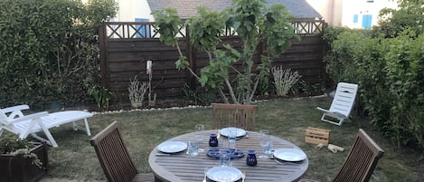 A round wooden table set for four with chairs, surrounded by a garden with a wooden fence and plants.