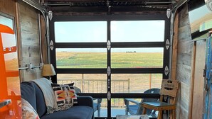 Un intérieur chaleureux avec un canapé, une table basse en bois et une vue sur un champ verdoyant, visible à travers une grande fenêtre.