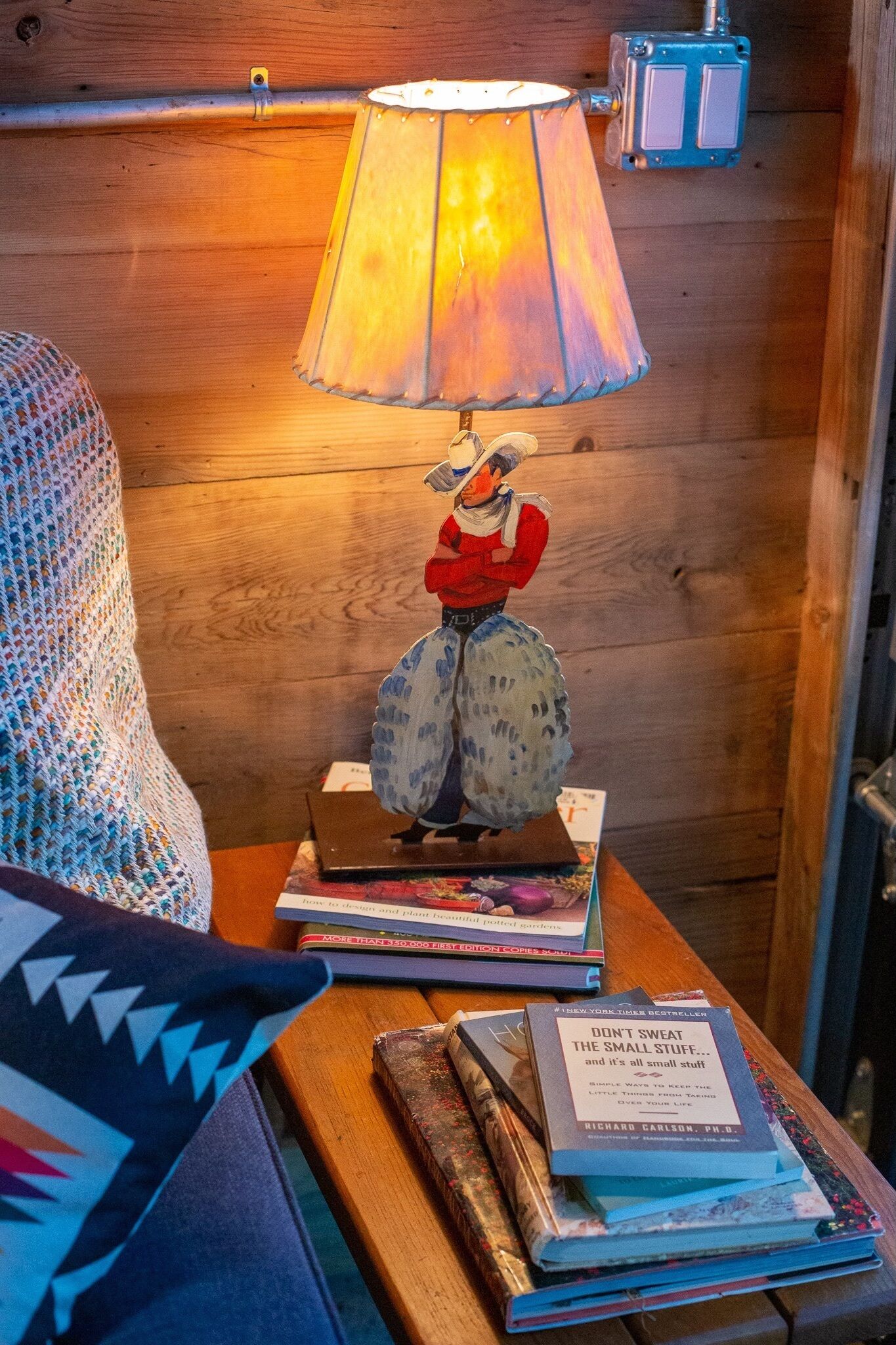 Uma mesa de madeira com uma luminária, livros e uma figurinha.