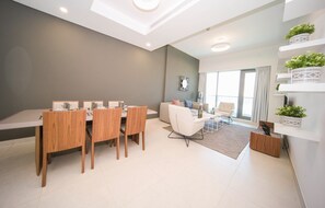 A modern living room with a dining area, large windows, and built-in shelving with plants. - Business Bay 1BR Canal View Rooftop Pool - 360 vacation (Dubai)