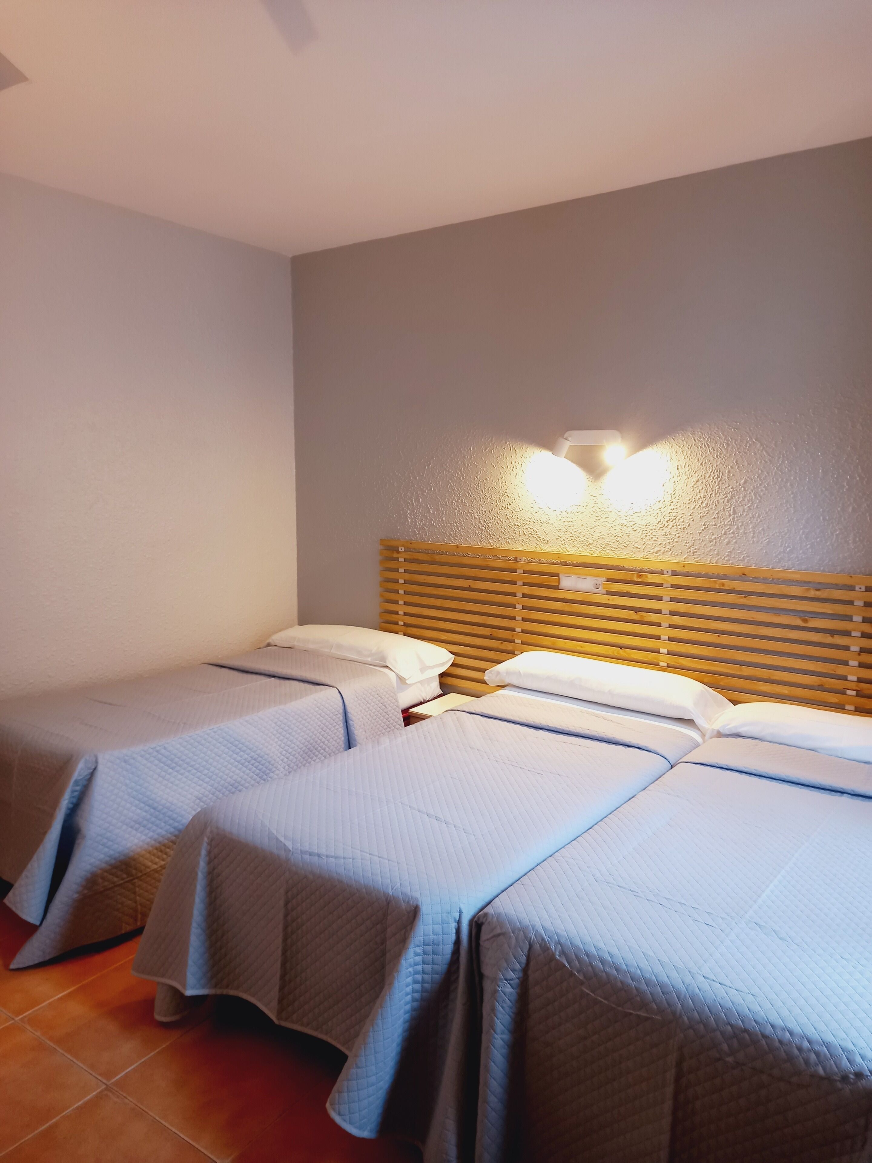 Habitación de hotel con dos camas individuales, cabecera de madera y una lámpara fijada a la pared.