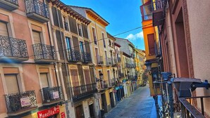 Une rue étroite bordée de bâtiments des deux côtés, un café avec des tables en terrasse et une enseigne indiquant « Manolita ».