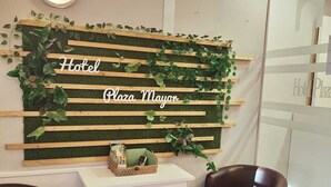 Un espace d'accueil avec un mur en lambris de bois sur lequel est inscrit « Hôtel Plaza Mayor », ainsi qu'un bureau blanc surmonté d'un panier.