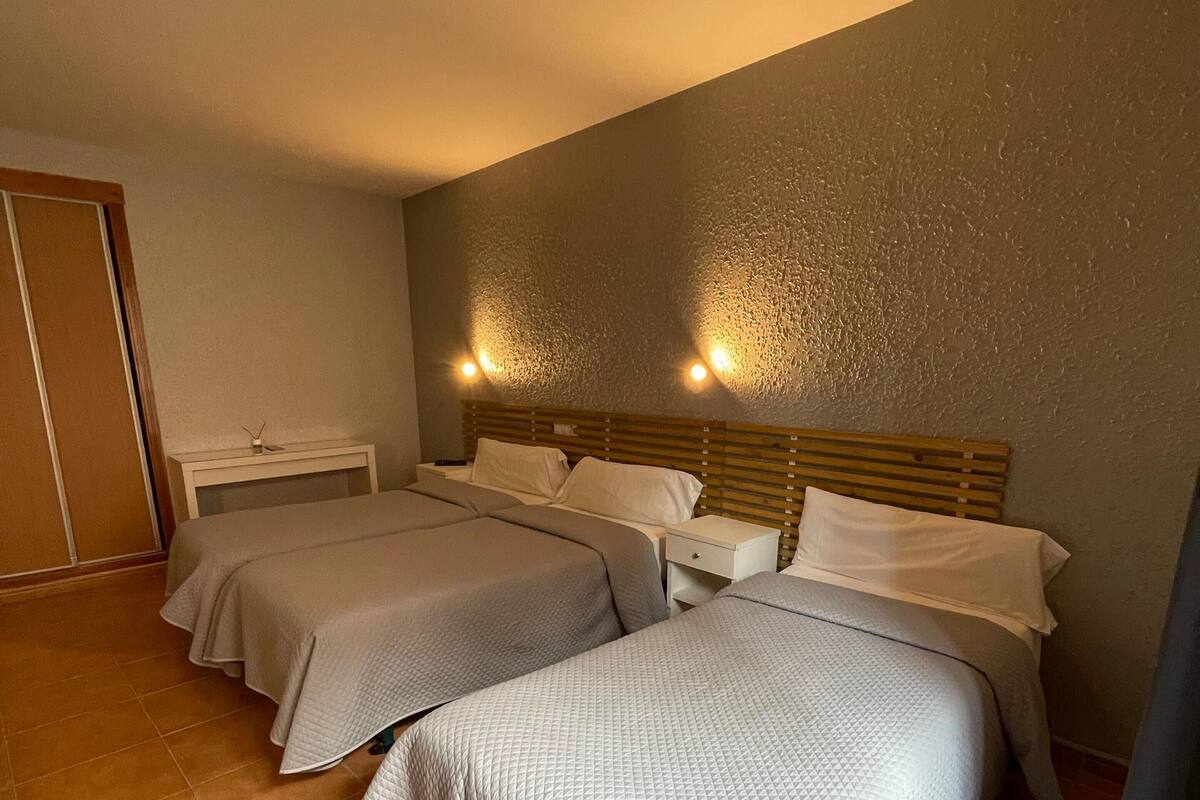 Habitación de hotel con dos camas, una mesita de noche y una lámpara fijada a la pared.