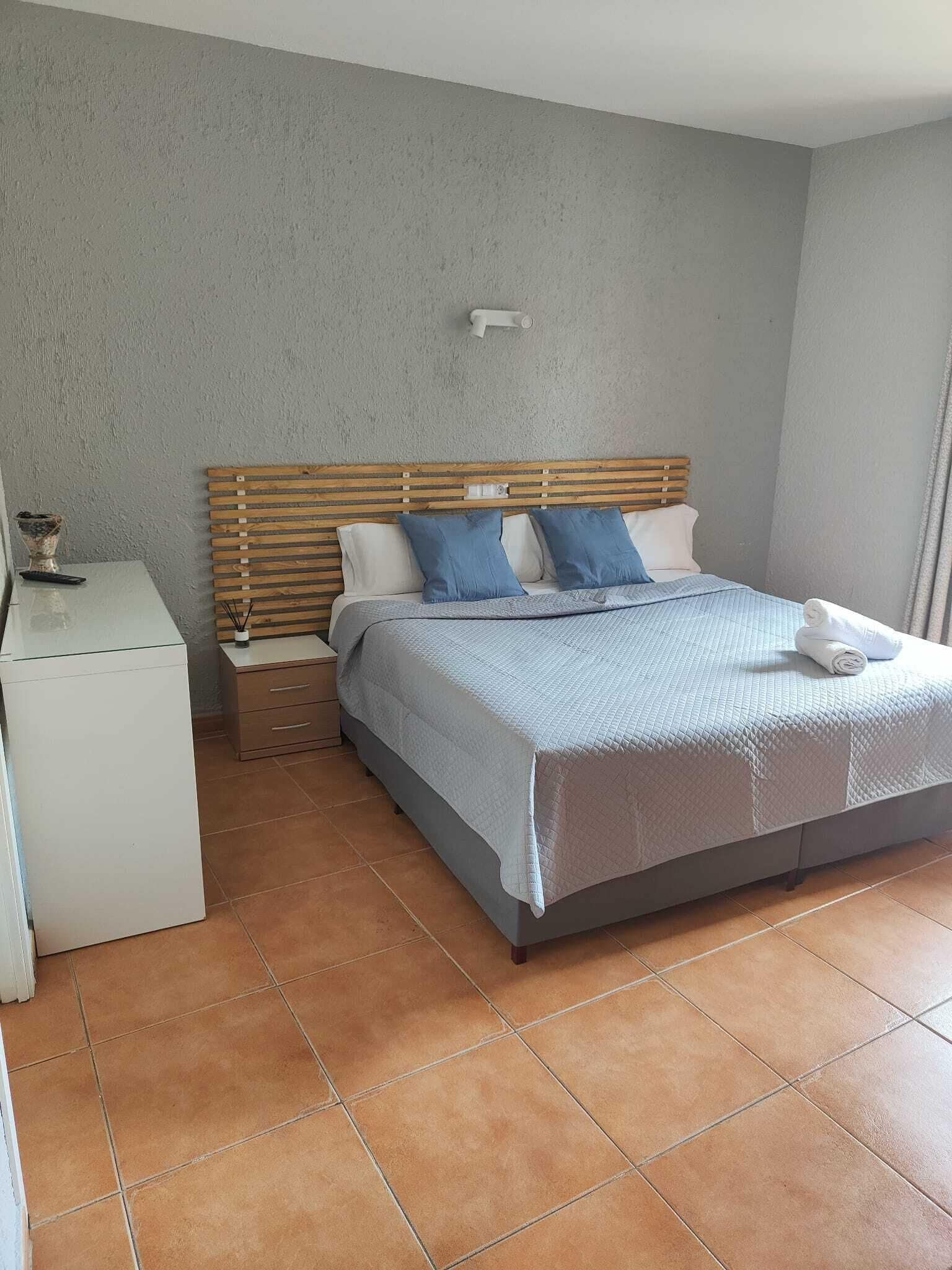 A bedroom with a bed, a nightstand, a small white cabinet, and a wall-mounted light fixture.