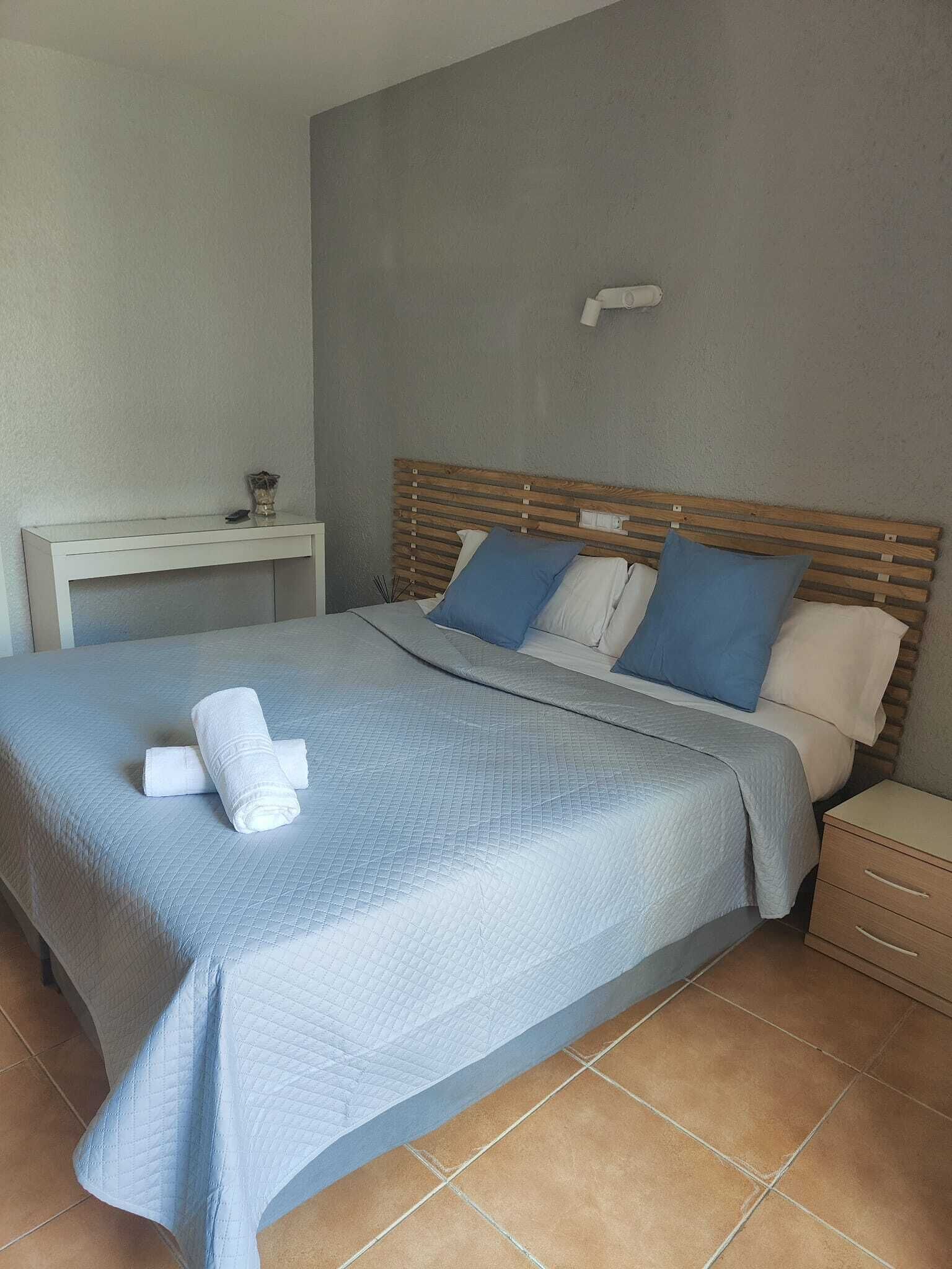 A neatly made bed with a blue quilt, a wooden headboard, and two bedside tables.