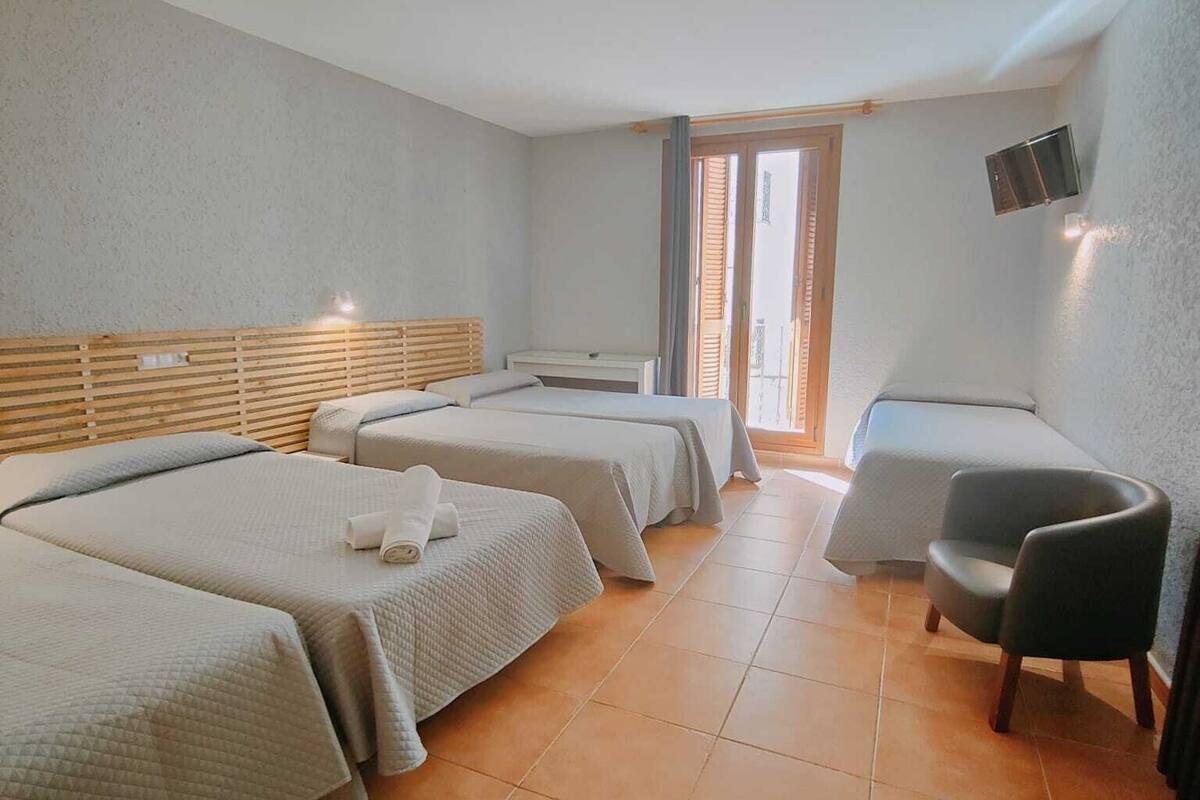Habitación de hotel con dos camas, una silla, un televisor y una ventana con persianas.