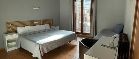 Un dormitorio con cama, mesita de noche, silla, escritorio y televisor montado en la pared.
