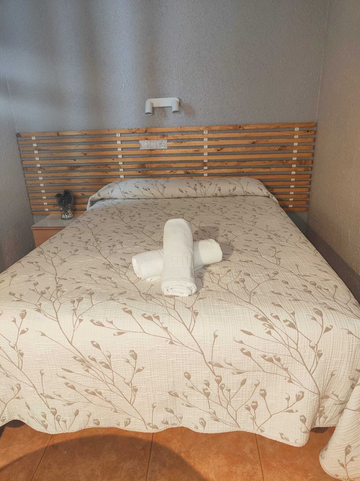 En snyggt bäddad säng med ett blommigt överkast och en hoprullad handduk i mitten.