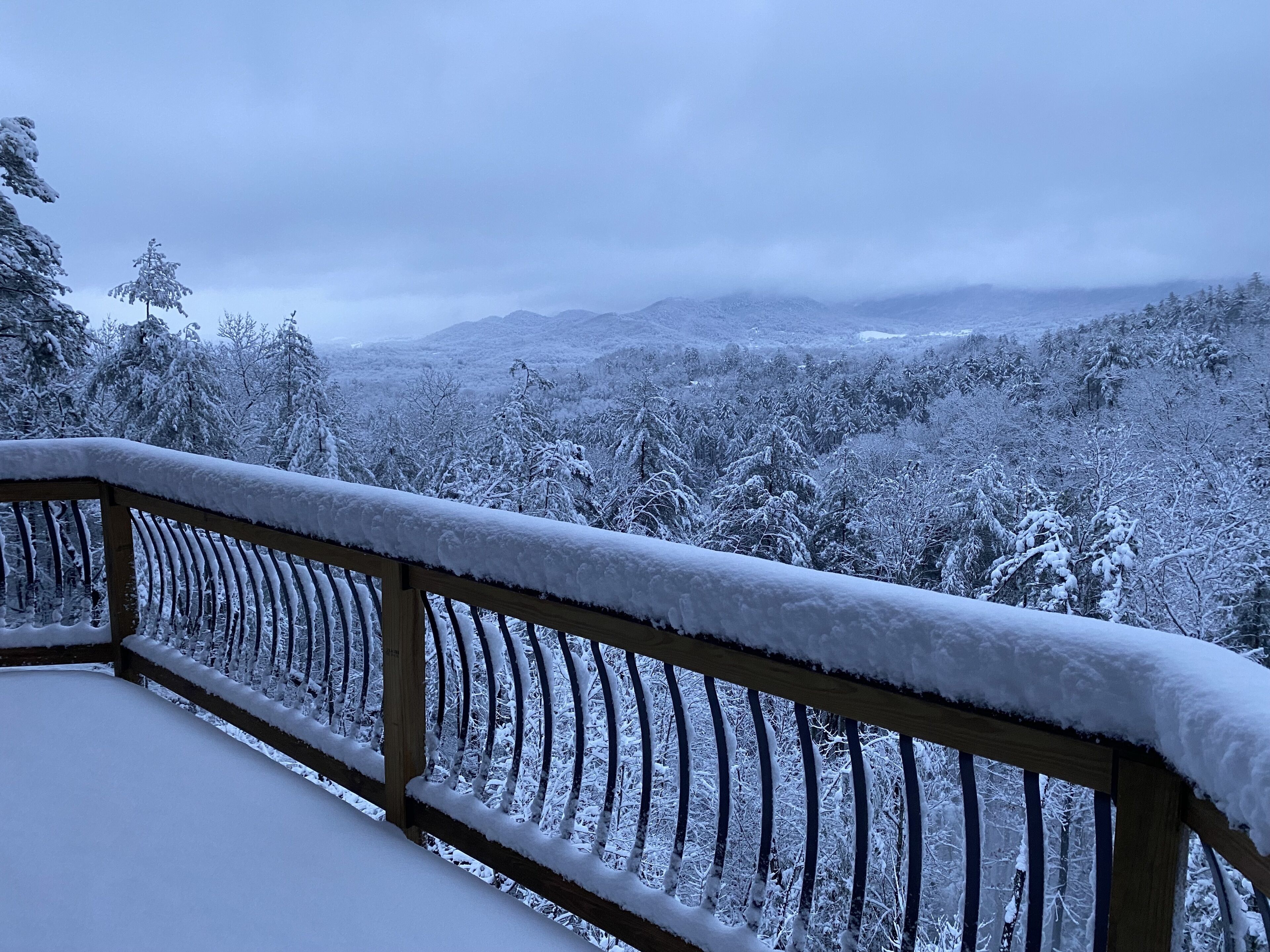 A snow-covered balcony with a view of a forested mountain range.