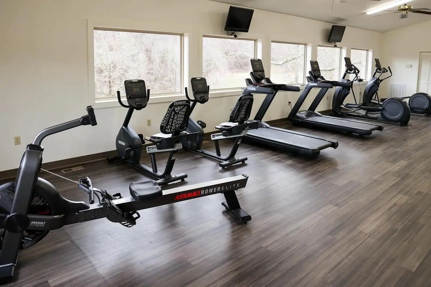 A gym with multiple cardio machines, including treadmills and stationary bikes, arranged in rows.