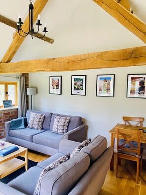 A living room with a grey sofa, a wooden dining table, and a chandelier. - Bright two bed cottage in  beautiful countryside with log burner. (Henley in Arden.)