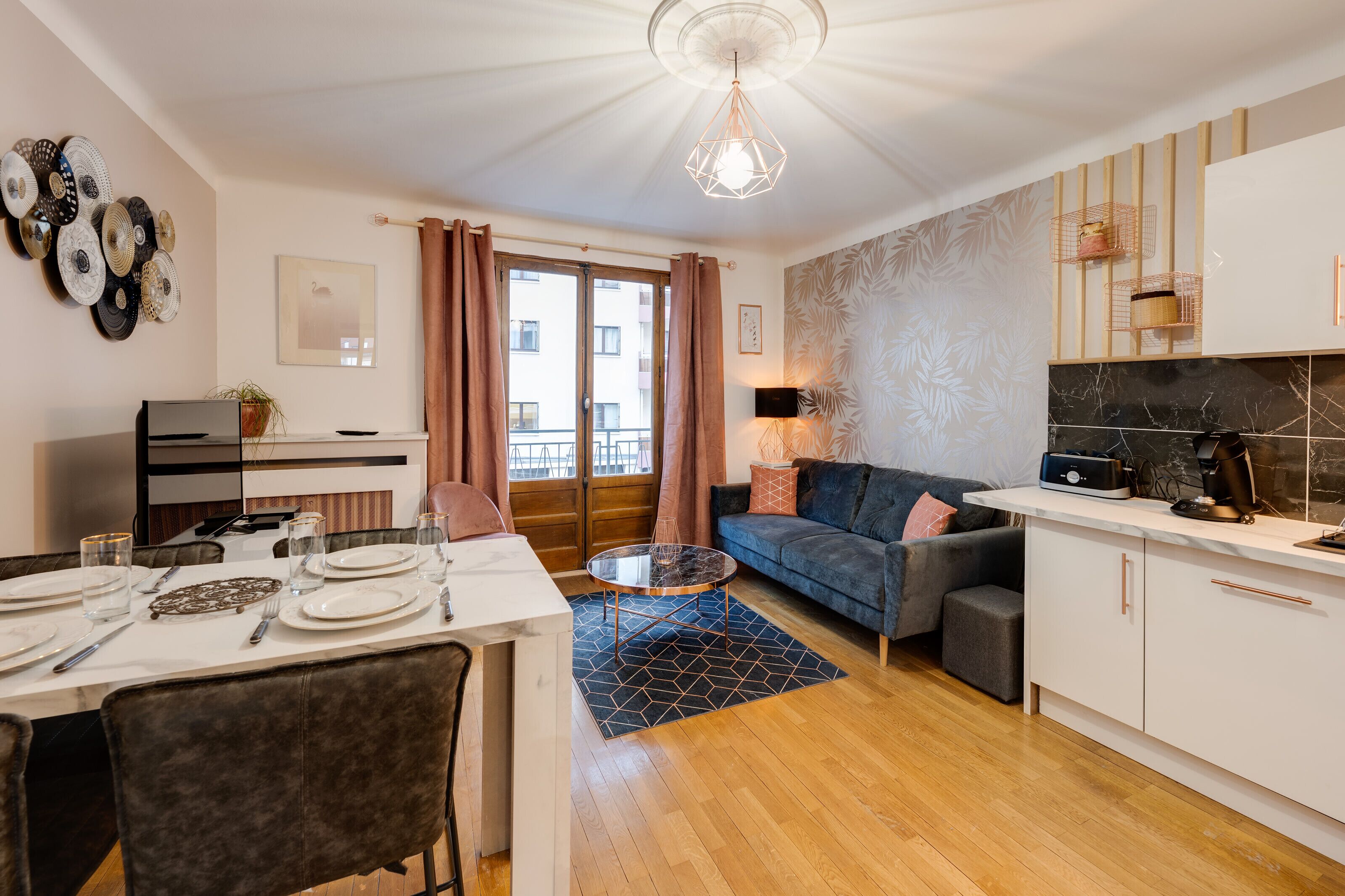 A modern living room with a sofa, a dining table set for four, and a kitchen area with a countertop and cabinets.
