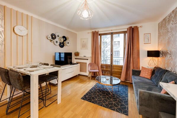A modern living room with a dining area, a fireplace, and a large window with curtains. - Les Mulots - Apartment T3 of 56 sqm (Annecy)
