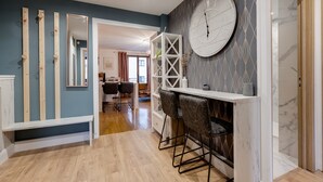 Una cocina moderna con barra integrada, vigas de madera, un reloj de pared grande y vista al área de comedor.