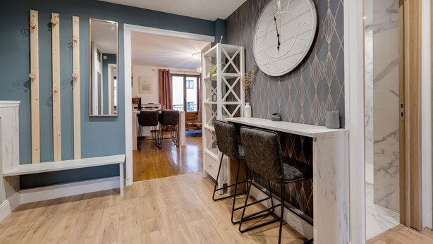 Una cocina moderna con barra integrada, vigas de madera, un reloj de pared grande y vista al área de comedor.