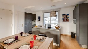 A modern kitchen with a dining area, featuring a wooden table set for four, a built-in oven, and a large window providing natural light. - Le Kaliste*** - apartment for 4 people + garage (Annecy)