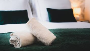 A neatly made bed with a green bedspread and two rolled towels.
