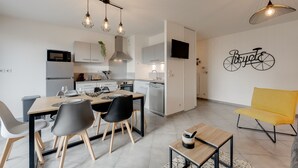 A modern kitchen with white cabinets, a dining area with a wooden table and chairs, and a yellow armchair. - L'Art de Ville*** - 2  bedroom near the city center, terrace and garage (Annecy)