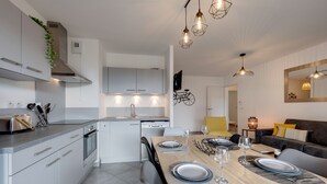 A modern kitchen with white cabinets, a built-in oven, and a dining area with a wooden table set for four. - L'Art de Ville*** - 2  bedroom near the city center, terrace and garage (Annecy)