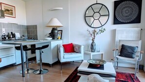 A modern kitchen with a dining area, white furniture, and decorative wall art. - Charming bright T2, balcony, parking, telework (Annecy)