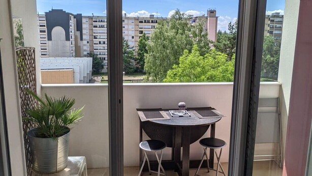 A balcony with a table and chairs, a potted plant, and a view of buildings and trees. - Charming bright T2, balcony, parking, telework (Annecy)