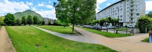 A residential area with a grassy field, a paved walkway, and a multi-story apartment building with parked cars. - Charming bright T2, balcony, parking, telework (Annecy)