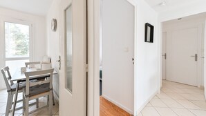 A room with a dining table, chairs, a clock, and a door leading to another room. - Le Boileau - Apartment for 4 people, parking and balcony, CLOSE to the Lake (Annecy)