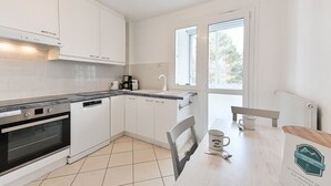 A modern kitchen with white cabinetry, a built-in oven, and a dishwasher. There is a dining table with a chair and a coffee maker. - Le Boileau - Apartment for 4 people, parking and balcony, CLOSE to the Lake (Annecy)