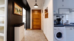 A narrow hallway with a wooden door, a washing machine, and a coffee maker in a compact kitchen area.