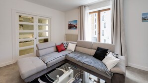 A modern living room with a sectional sofa, a glass coffee table, and a view of a cityscape through large windows.