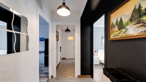 A hallway with a modern design, featuring a light fixture, a painting, and a desk with baskets.