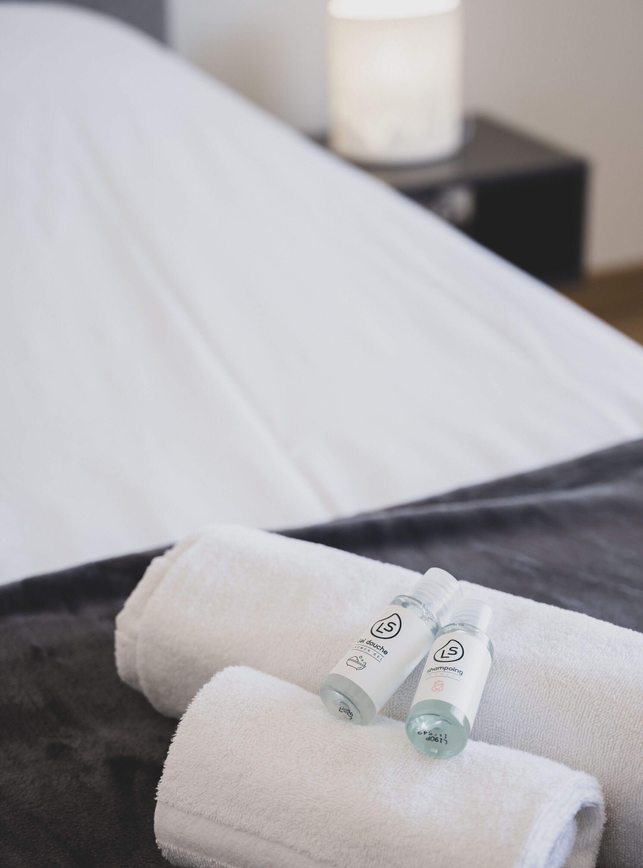 Een net opgemaakt bed met witte lakens en twee flesjes toiletartikelen op een witte handdoek.