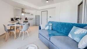 A modern living room with a blue sofa, a dining table with chairs, and a kitchen area with cabinets and appliances. - La Cantonade - Nice T2 with garage for 4 people near Beach (Annecy)