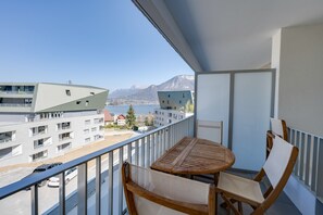 A balcony with a table and chairs, overlooking a lake and buildings.