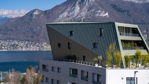 A modern building with a unique angular design, a balcony, and a view of a mountainous landscape and a body of water. - La Cantonade - Nice T2 with garage for 4 people near Beach (Annecy)