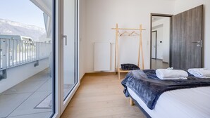 A modern hotel room with a balcony, a bed with a dark blanket, a wooden hanger rack, and a wardrobe. - La Cantonade - Nice T2 with garage for 4 people near Beach (Annecy)