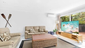 Een woonkamer met een beige bank, een houten salontafel en een televisie waarop een strandscène te zien is.