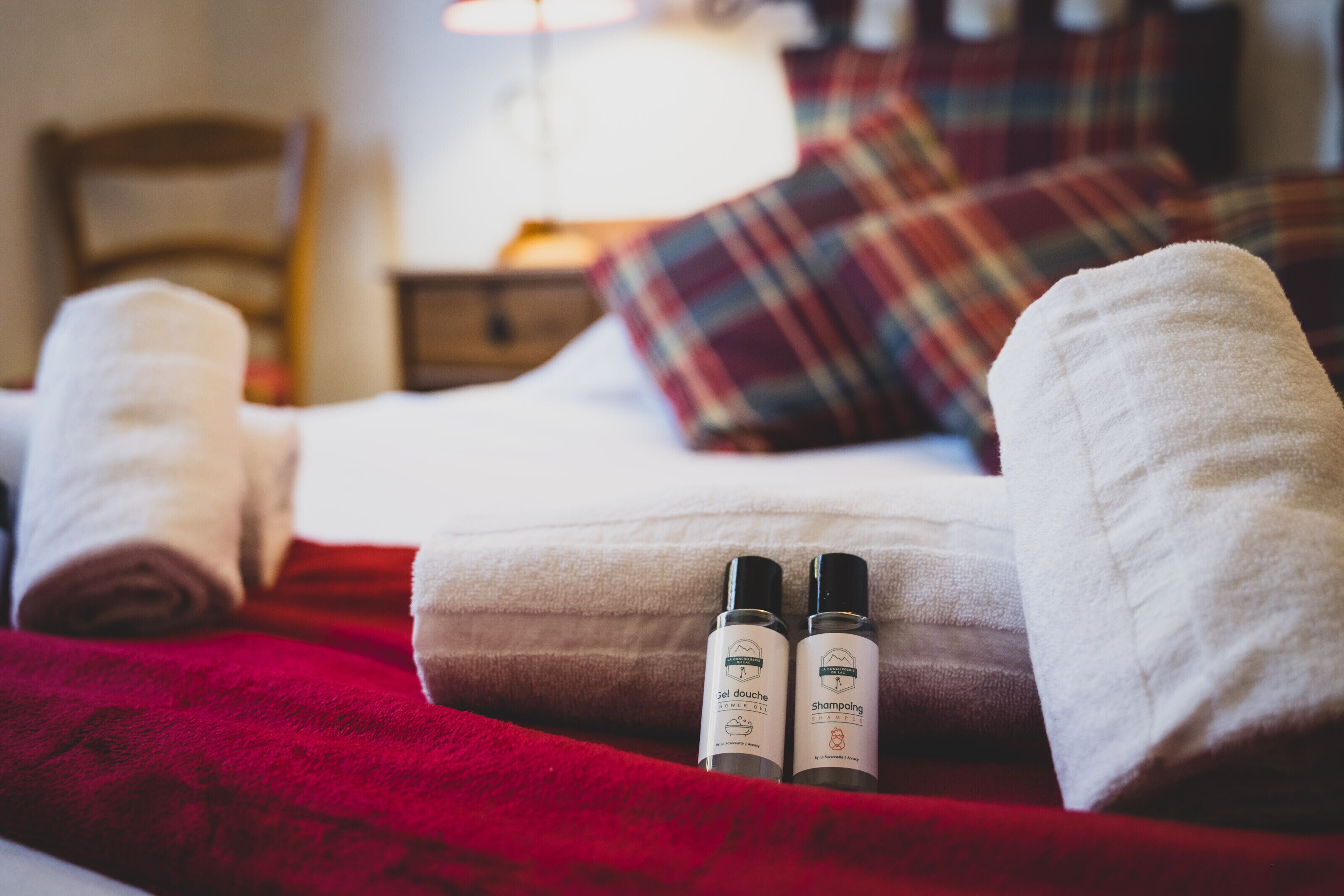 A neatly made bed with rolled towels and two bottles of shower gel and shampoo.