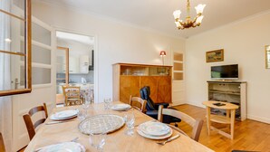 A dining area with a wooden table set for four, a television, and a bookshelf. - T2 of 55sqm for 3 people (Annecy)