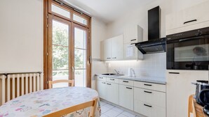 A kitchen with a dining table, cabinets, a stove, and a window. - T2 of 55sqm for 3 people (Annecy)