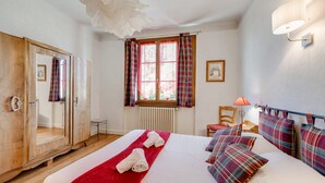 A hotel room with a large bed, a wardrobe, a window with curtains, a radiator, a lamp, and a chair. - T2 of 55sqm for 3 people (Annecy)