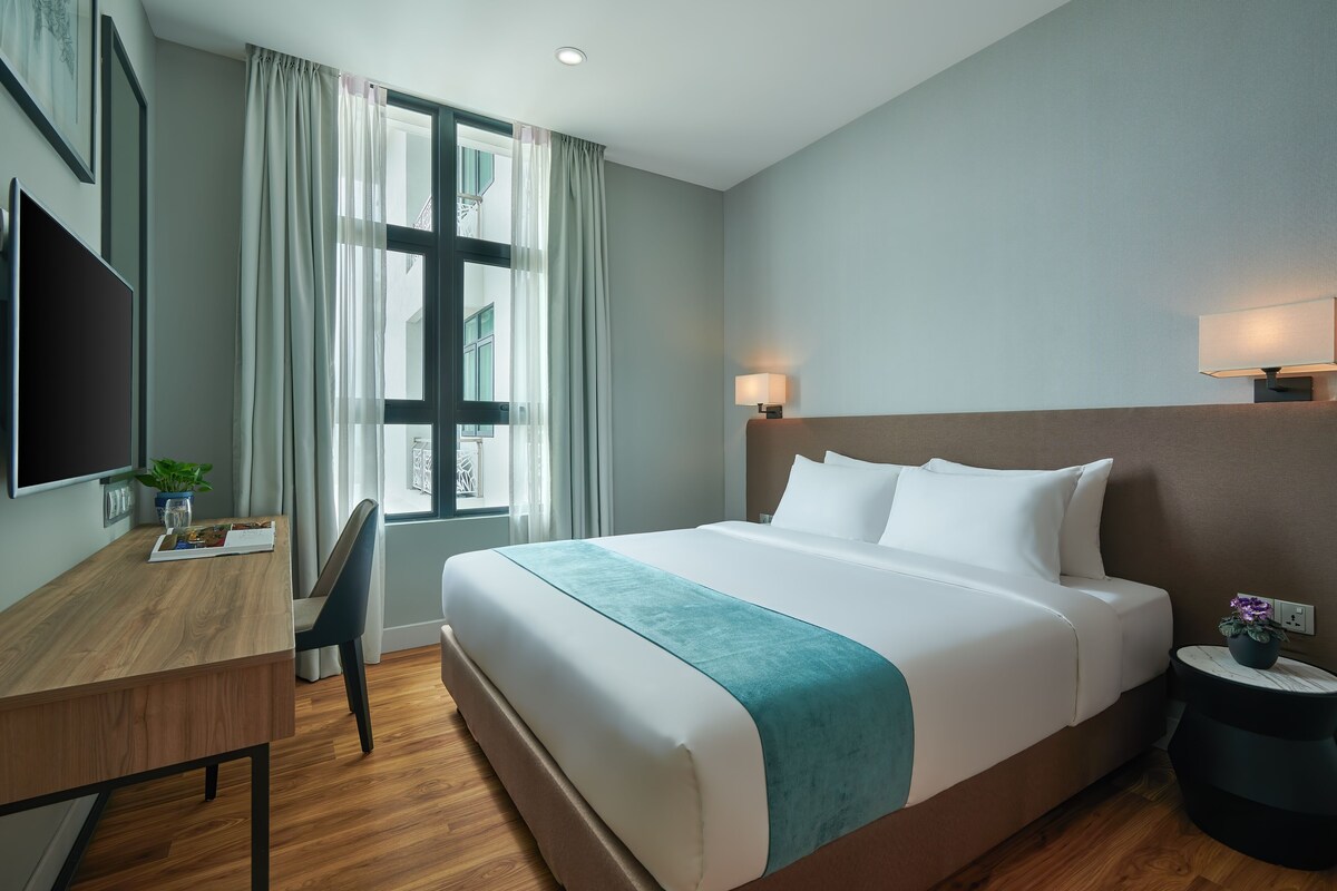 Ein Hotelzimmer mit einem großen Bett, einem Schreibtisch mit Stuhl, einem Fernseher und einem Fenster mit Vorhängen.