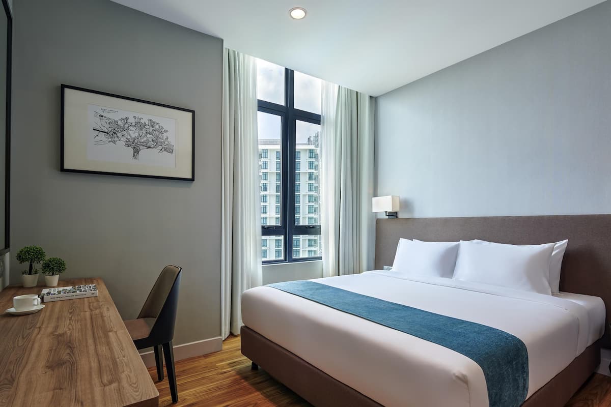 Une chambre d’hôtel avec un lit, un bureau, une chaise, un tableau encadré et une fenêtre donnant sur la ville.