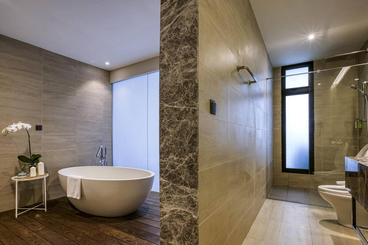 Une salle de bain moderne avec une baignoire sur pieds, une petite table d’appoint agrémentée d’une plante et une grande fenêtre.